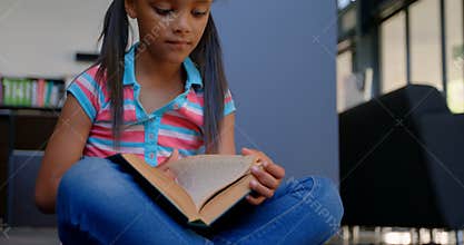 Front view of attentive African American schoolgirl reading a book in library at school 4k