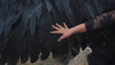 Light tender hand is holding a hand over a black strong wing, the daughter of an angel and a demon is sitting on the