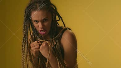 Angry woman with dreadlocks boxing front camera in studio on yellow background