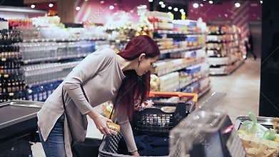 Young beautiful woman with stunning earings and red hair is laying out products on a checkout count in a grocery store.