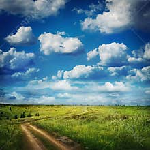 Summer country road and fields of the blue beautiful cloudy sky.