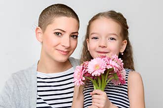 Happy Mother`s Day, Women`s day or Birthday background. Cute little girl giving mom, cancer survivor, bouquet of pink daisies.