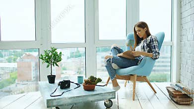 Young attractive woman read book and drink coffee sitting on balcony in modern loft apartment