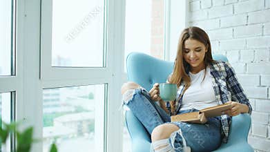 Young attractive woman read book and drink coffee sitting on balcony in modern loft apartment