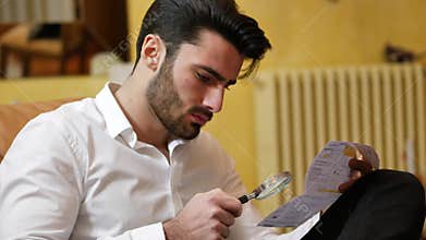 Young man examining contract or bill with magnifying glass