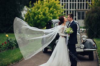 stylish bride and groom sensually posing near retro car with boh