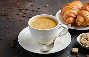 Cup of fresh coffee with croissants on dark background