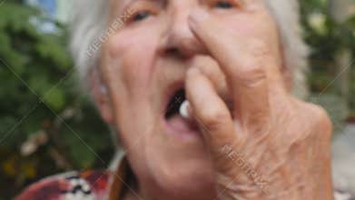 Old woman holding white pill in her hand and take it. Grandmother putting tablet in her mouth. Healthcare and medical