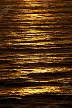 Rippled ocean surface glows with rich copper color at sundown