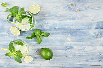 Tropical fresh cold cocktail gin tonic with mint, lime, ice, straw on light blue shabby wood board, border, top view.