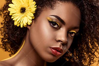 Close-up portrait of young sensual african american woman with artistic make-up and gerbera in hair