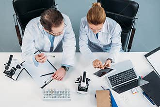 overhead view of scientific researchers in white coats using tablet together at workplace