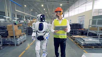 Human factory worker and a robot are walking together in factory premises