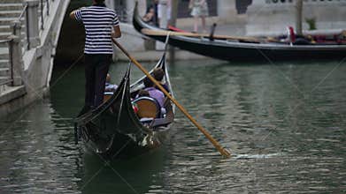 Male gondolier riding curious tourists on canal, showing attractions of Venice