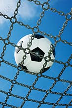 Soccer ball in chain net white and black football, blue sky