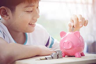 Asian Little boy saving money in pink piggy bank.