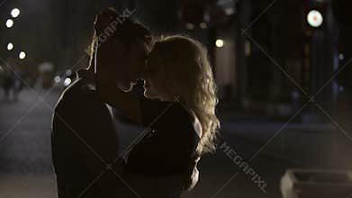Blond female teasing and cuddling boyfriend in the night street, silhouettes