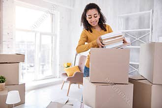 Cute curly-haired girl packing books before moving out