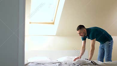 Happy man making bed at home