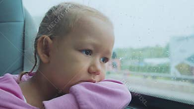 Portrait of sad child looking out the wet window, while travelling by bus.