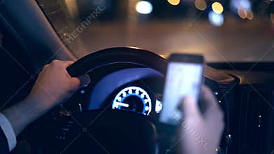 Unrecognizable man driving car at night and web surfing phone danger concept