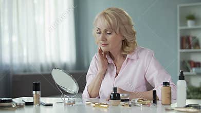 Middle-aged woman looking in mirror at face after skin rejuvenation procedure