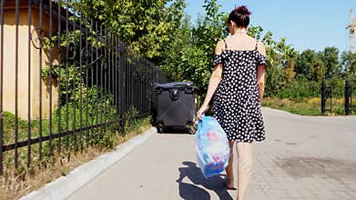 Back view, girl is carrying a package of garbage in her hands, throwing out trash. summer hot day. ecology. separation