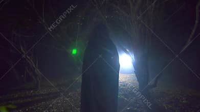 A figure in a black robe with a candle goes through a mysterious forest