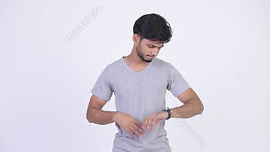 Young stressed bearded Indian man checking time while looking bored