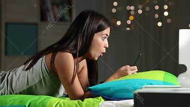 Surprised teen watching media in a phone on a bed