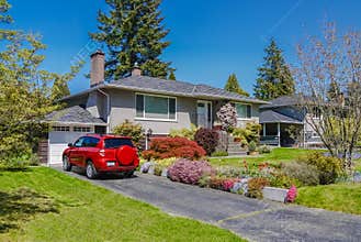 Modest residential house with red car parked on driveway in front. Family house with blossoming flowers on the yard