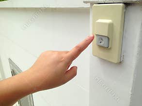 Woman`s hand push the doorbell in front of house.