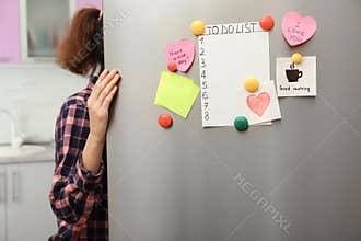 Woman opening refrigerator door with paper sheets