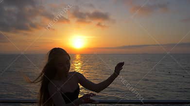 SLOW MOTION. Beautiful ballerina performing pirouette. Blonde woman in black ballet tutu on embankment above ocean or