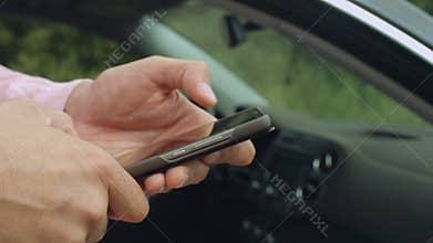 Male hands text messaging on cellphone near car