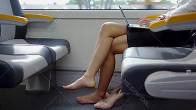 Barefoot woman works with laptop in train