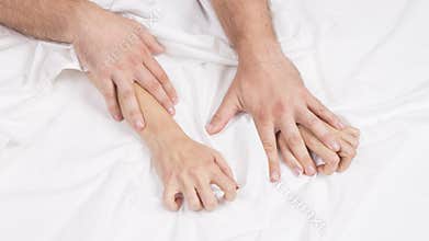 Sensual beautiful young couple is having sex on bed. Female hand pulling white sheets in ecstasy, orgasm. Love concept