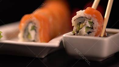 Sushi roll with chopsticks dipped in soya sauce