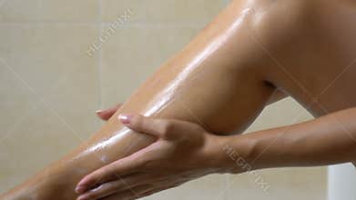 Woman applying lotion after waxing legs in bathroom, hair removal and skin care