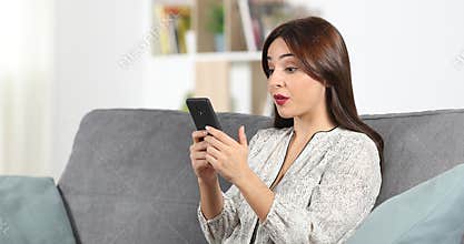 Surprised woman reading phone content at home