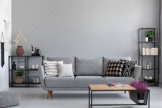 Metal black shelves with books, candles and plants behind the grey sofa with patterned pillows, real photo with copy space
