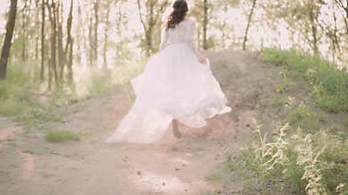 Young slim and attractive girl in elegant white vintage dress with a long fluttering train and flying dark wavy hair in