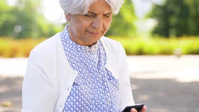 Senior woman taking smartphone out of bag in park