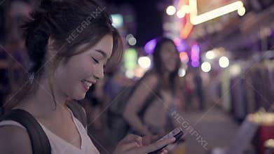 Asian woman tourist backpacker smiling and using smartphone traveling alone holidays outdoors on city street.