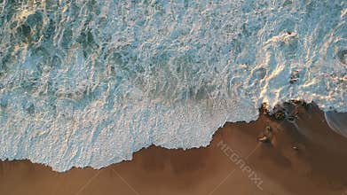 Aerial overhead rough white waves crashing on rocks on beach