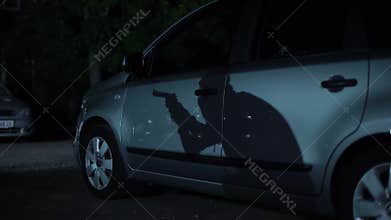 Shadow of gangster with gun walking on dark parking night, high-crime city area