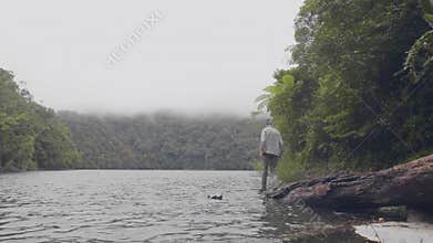 Traveling man standing on tree falling in river water in tropical forest on green highlands background. Young man
