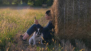 Young woman sitting at the meadow with french bulldog