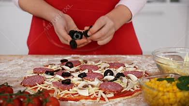 Young girl hands scatter olive slices on pizza prepared at home