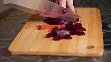 Cutting boiled beets. Female hands are cutting boiled beets with a large knife on a wooden cutting board